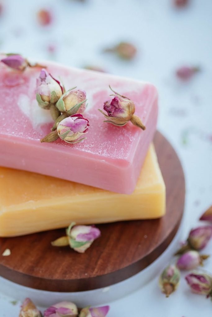 Artisan pink and yellow soaps with rose buds on wooden stand.