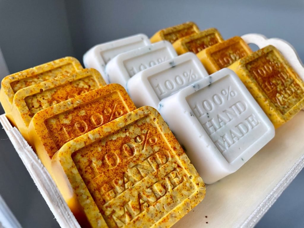 Handmade artisan soaps with 100% Hand Made text, showcasing organic ingredients and craftsmanship.