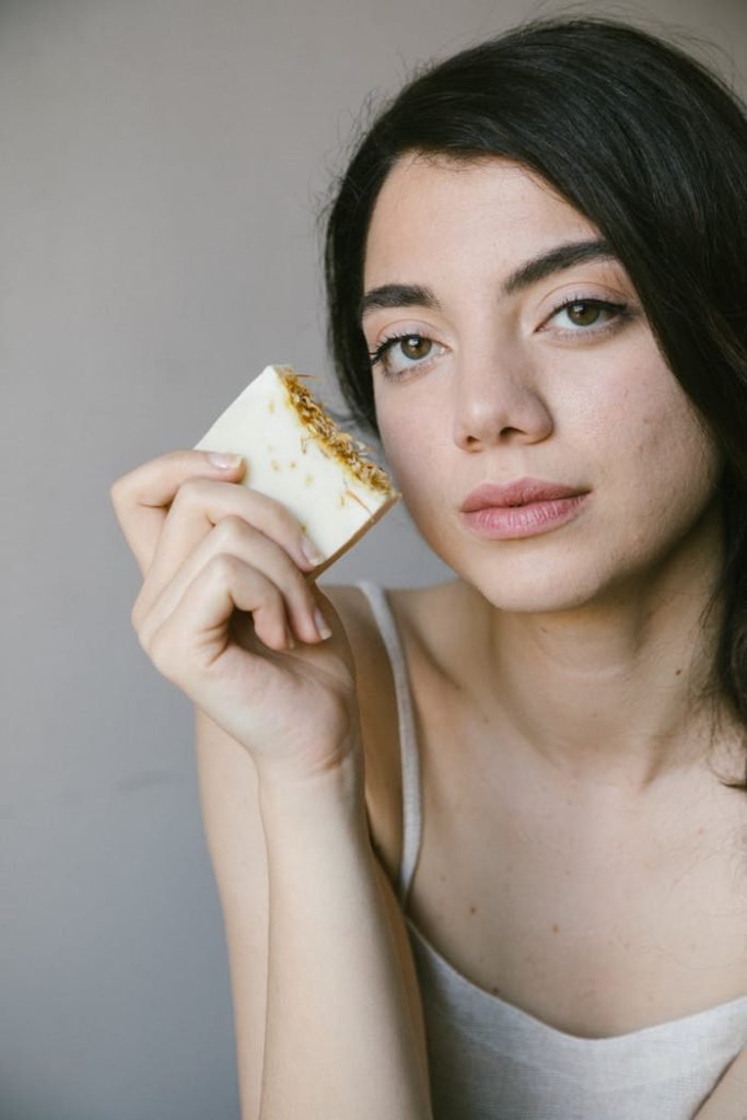 Woman holding natural soap bar near face, showcasing eco-friendly skincare in soft natural light.